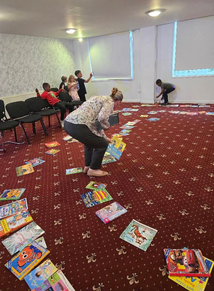Adult bending down with children and books scattered on floor