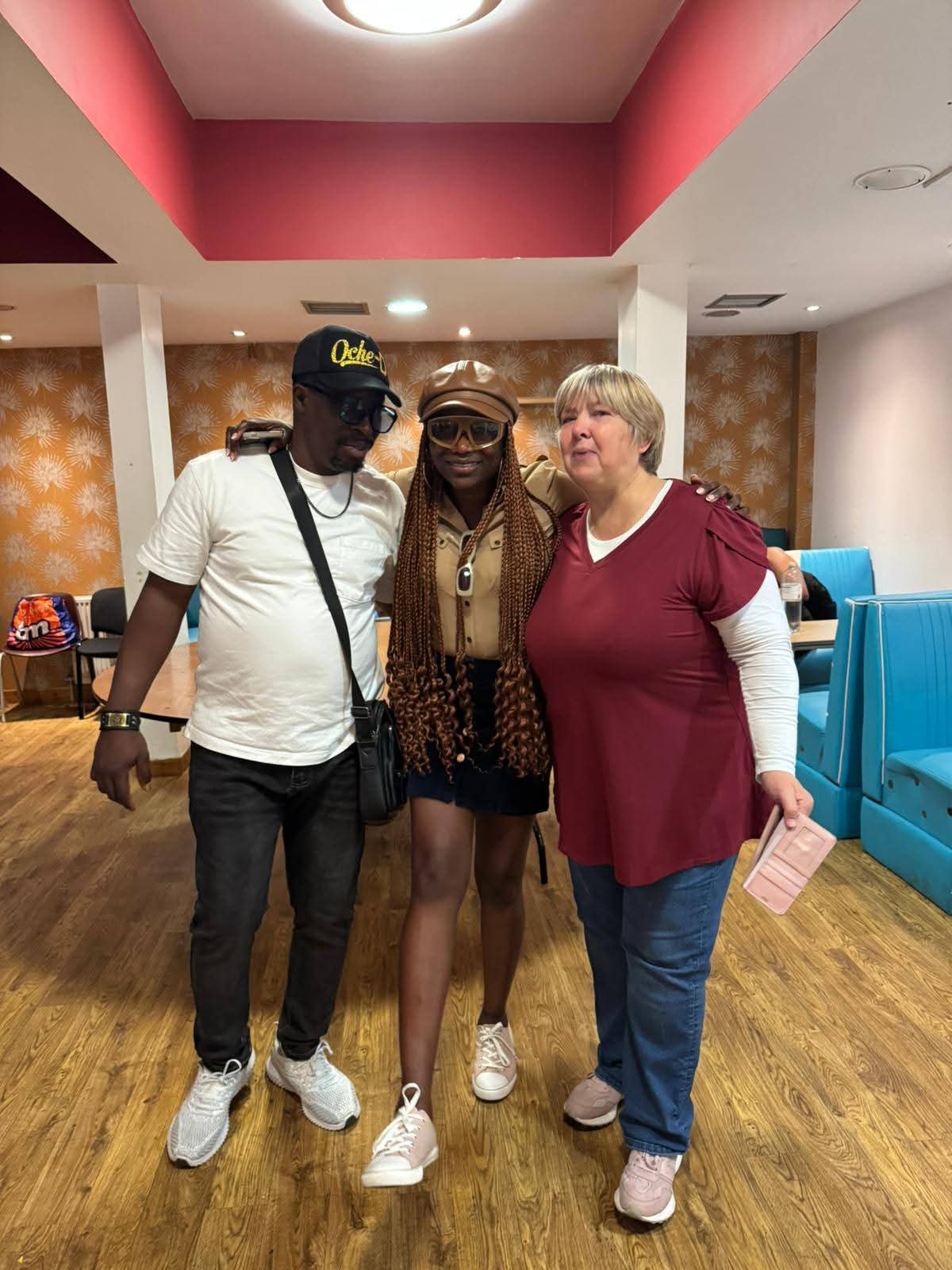 Three people posing together at indoor event with pink ceiling